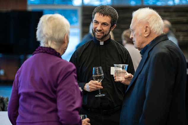 Father Ryan talking to a couple and drinking wine at the 2024 Crozier Lenten Retreat